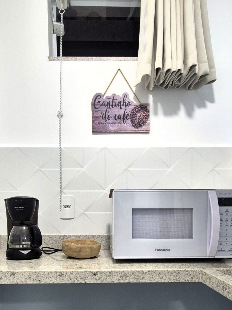 Detalhe da mini cozinha com cafeteira elétrica, micro-ondas e placa decorativa Cantinho do Café.